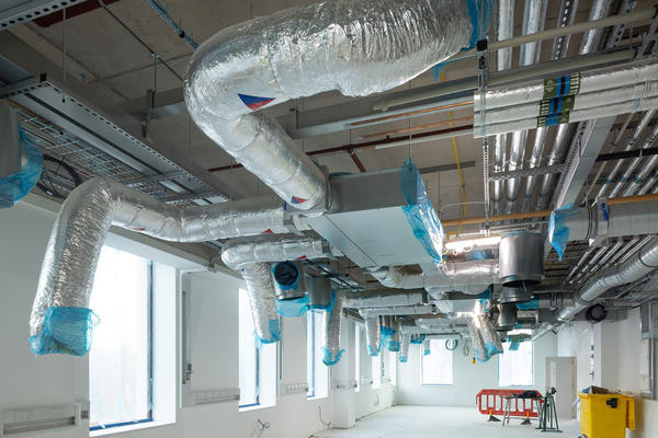 Interior view of exposed and insulated pipework within the Life and Mind Building, in an area with large windows and white-washed walls